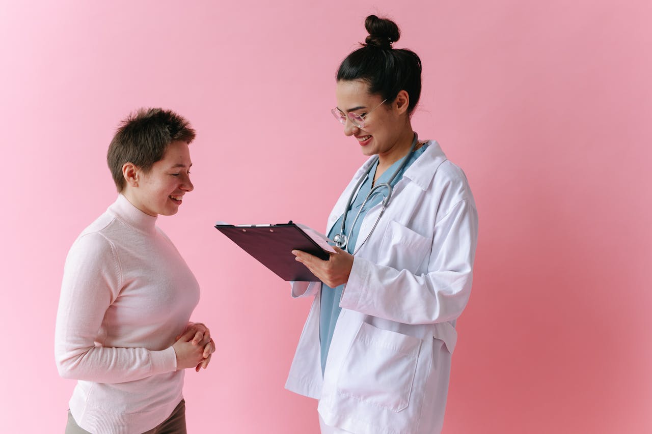hero-img-02 A doctor in a white coat consults a smiling patient against a pink backdrop.